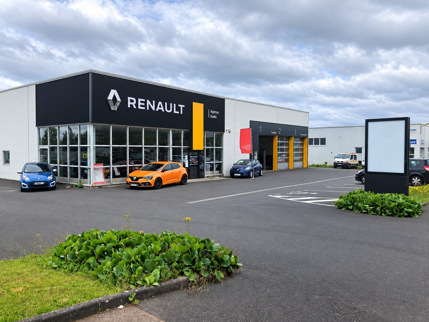 Façade d'une agence Renault avec une Mégane orange et d'autres voitures stationnées devant les vitrines, sous un ciel nuageux.