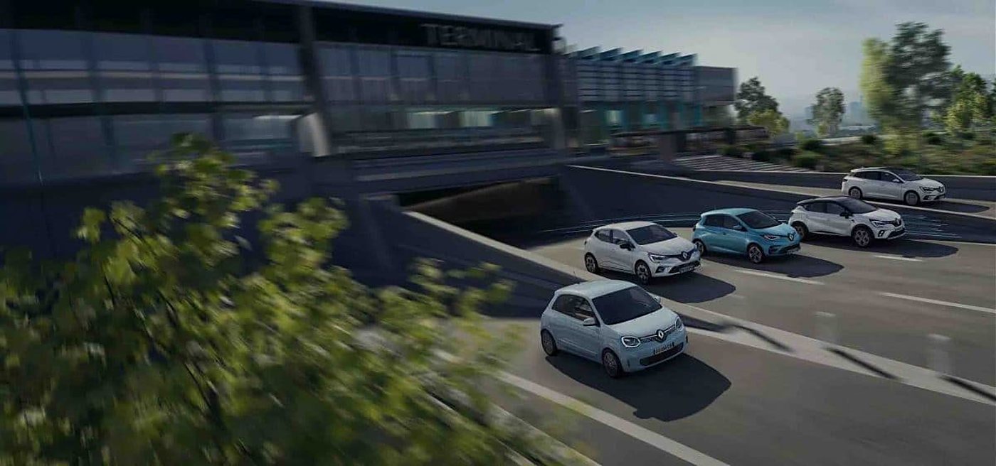 Cinq voitures Renault de couleurs claires circulent sur une route en courbe devant un bâtiment moderne en verre, avec du feuillage flou au premier plan.